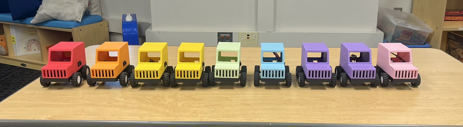 Nine 3D-printed cars in rainbow colors lined up on a classroom table